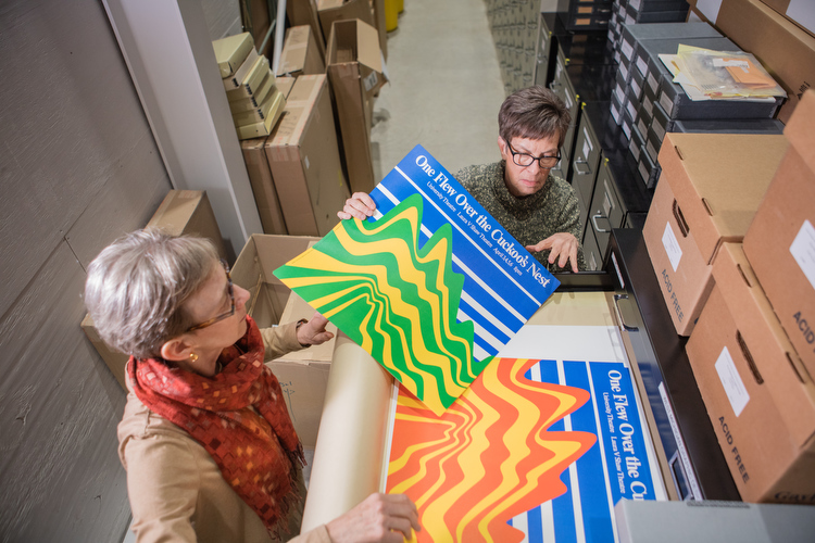 Barbara Loveland and Linda Powell look at old theater posters printed on colored paper.