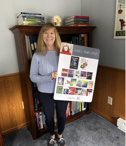 Nath in her writing cottage with a poster that was displayed at a recent book launch. (Photo/Courtesy of Judi Nath)