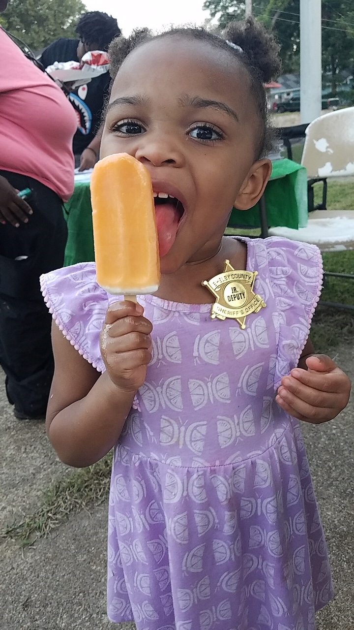 Un "subalterno" disfruta de una delicia en el evento National Night Out de Holmes Street. Los lÃ­deres comunitarios dicen que mejorar las relaciones con la policÃ­a es un componente clave para la seguridad del vecindario. (Madeline Faber)