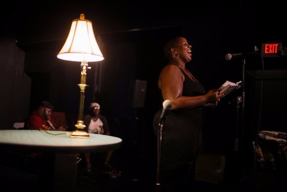 A local artist performs for a crowd at The Den from a notebook of original pieces.