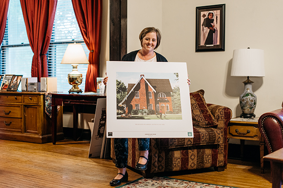 Tracy Burgess poses with a rendering of one of the properties Dorothy Day House will acquire.