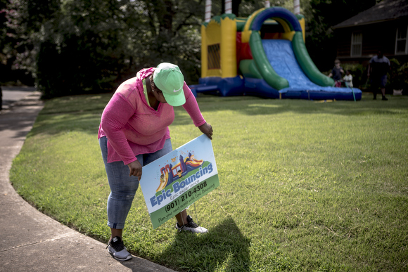 LaTonya Taylor, owner of Epic Bouncing, plants a sign in a client's yard while setting up a bounce house. She started her business with support from the RISE Foundation.