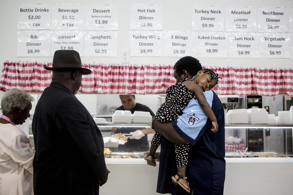 Carl Merriweather carries his sleeping granddaughter Arianna while ordering his plate from the line at Miss Shirley's in South Memphis.