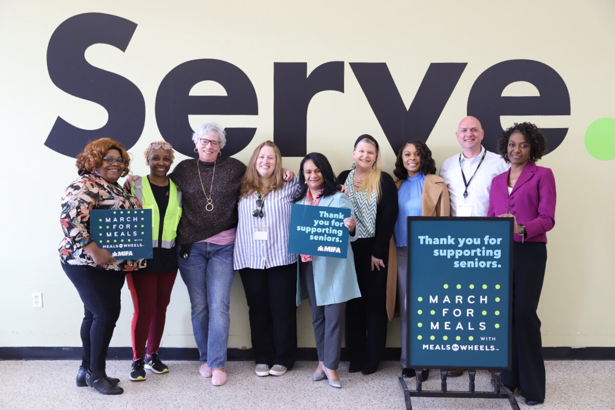 "The Meals on Wheels program is more than a meal," says Arnetta Stanton Macklin, Chief Engagement and Advocacy Officer for MIFA. She's pictured here in the center of a group of MIFA staff and volunteers. To the left of Arnetta is MIFA Director of Impact & Communications Ellen Whitten, who says, "Not all, but for a number of our clients, the volunteers, or the staff members who deliver their meals, are the only person they see all day. So to break that isolation and to give them a social connection and for them to know that somebody is going to come to check on them that day and is going to bring them a hot meal – it's so important."