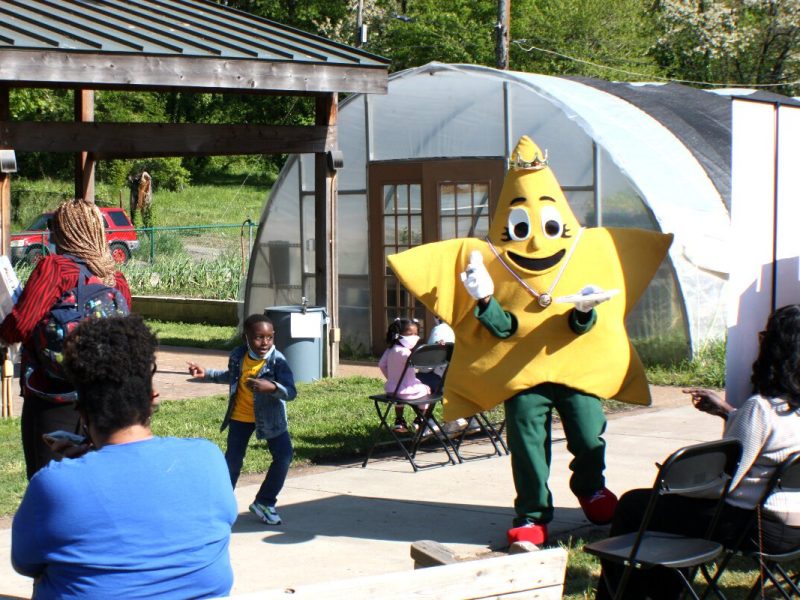 A young party goer and the mascot of the Paint It Clean bath kit dance to the music of the Jazz Brothers at the first Green Leaf Learning Farm Earth Day tour and tasting event, held on April 22, 2021. (Cole Bradley)