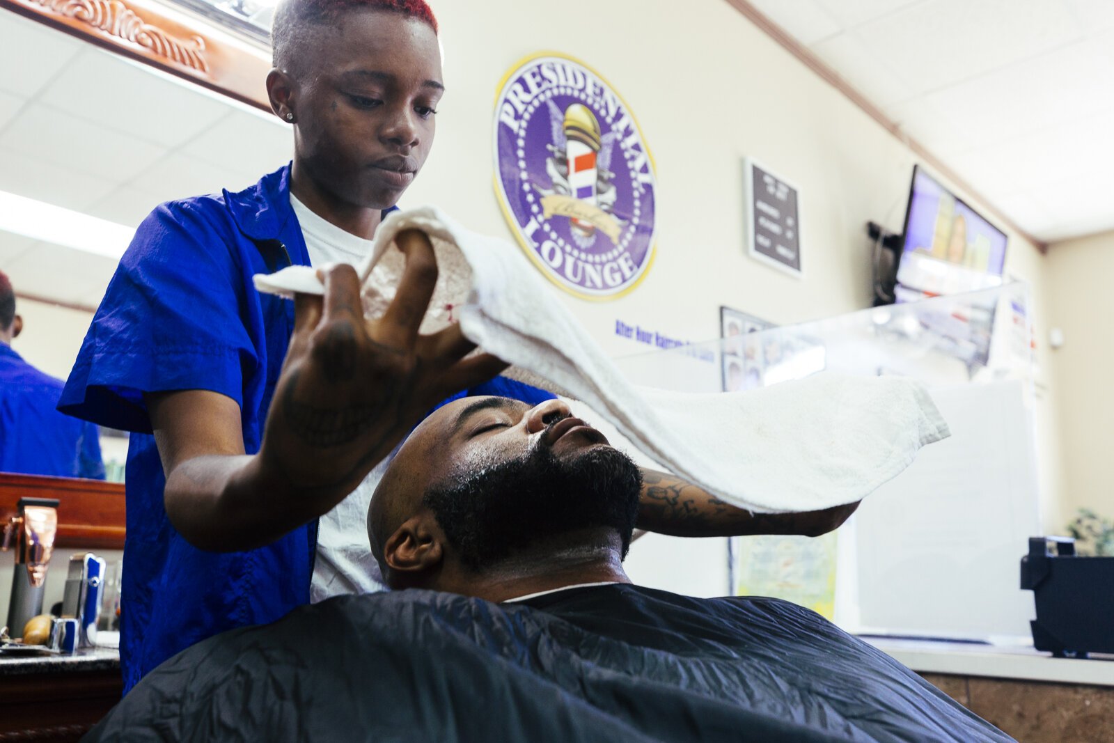 Wise Tardezia performs a single blade razor shave and towel facial treatment on Pedro Bateman at the Presidential Lounge Barbershop in Madison Heights. 2019. (Ziggy Mack)
