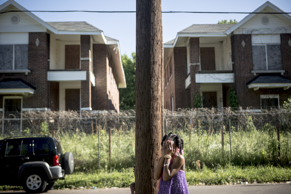 A young girl plays hide and seek in front of shuttered apartment buildings on Tate Street. 2017. (Andrea Morales)