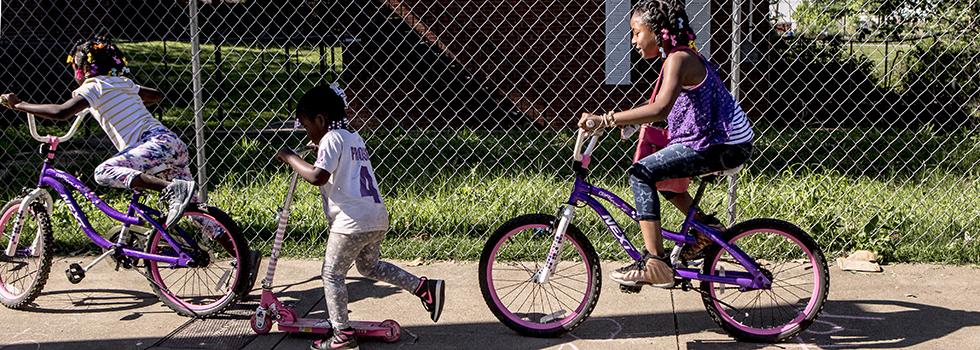Children take a ride down Tate Avenue in South Memphis. Behind them sits a vacant apartment building. (Andrea Morales)