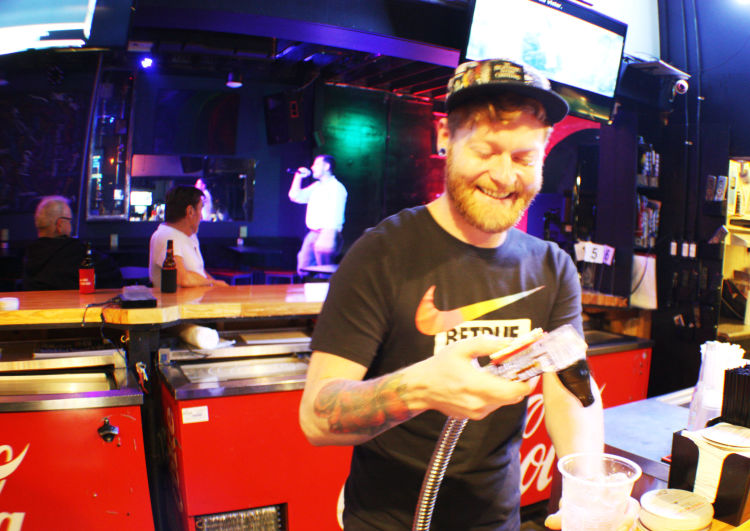 Dru's Bar bartender Bradley Moore pours a drink while a patron sings karaoke on the bar's catwalk. (Cole Bradley) 