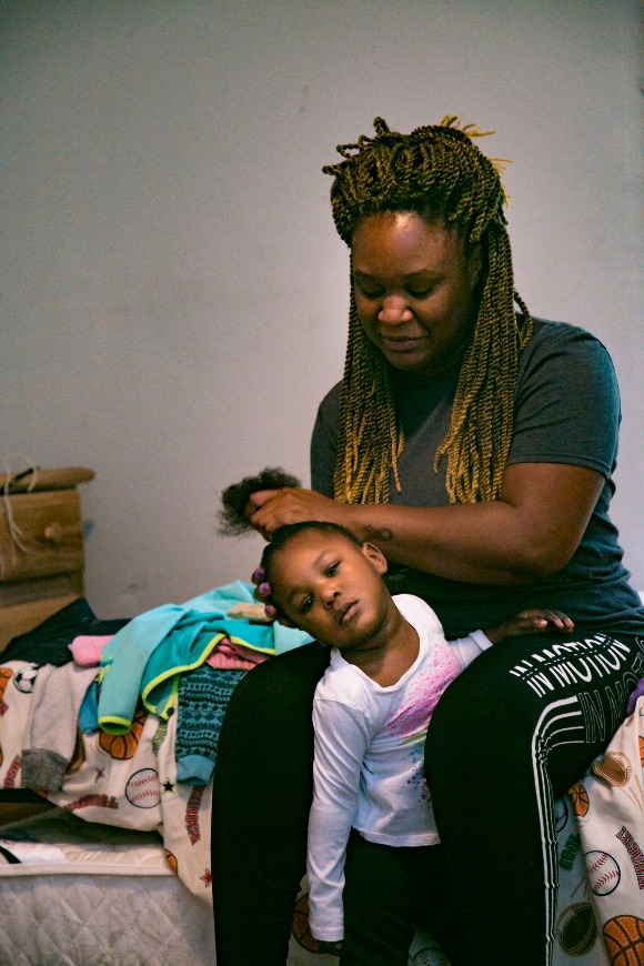 Daria Meeks fixes her two-year-old daughter's hair in the family's home. (Natalie Eddings)