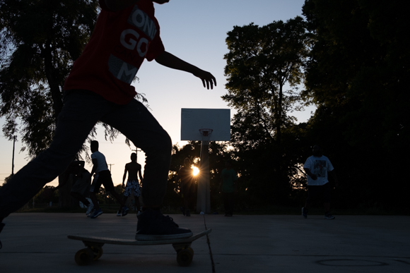 A boy rides by on a skateboard while young men play basketball in Booker T. Washington park. (Brandon Dahlberg)